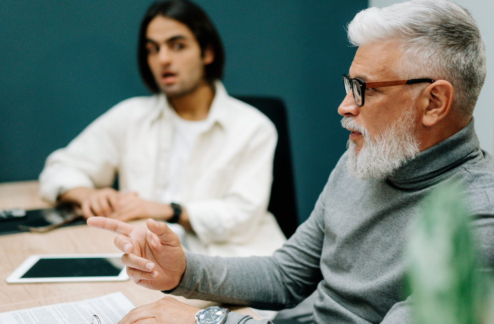 older male worker sitting at a desk with a younger male in a meeting