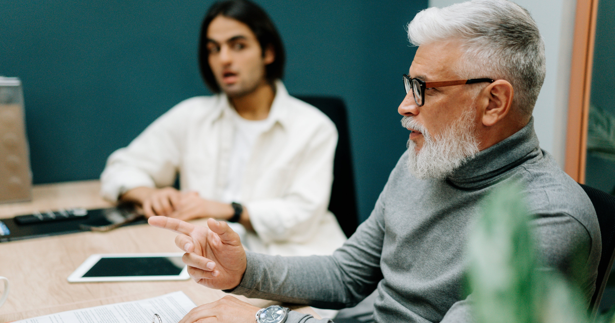 older male worker sitting at a desk with a younger male in a meeting